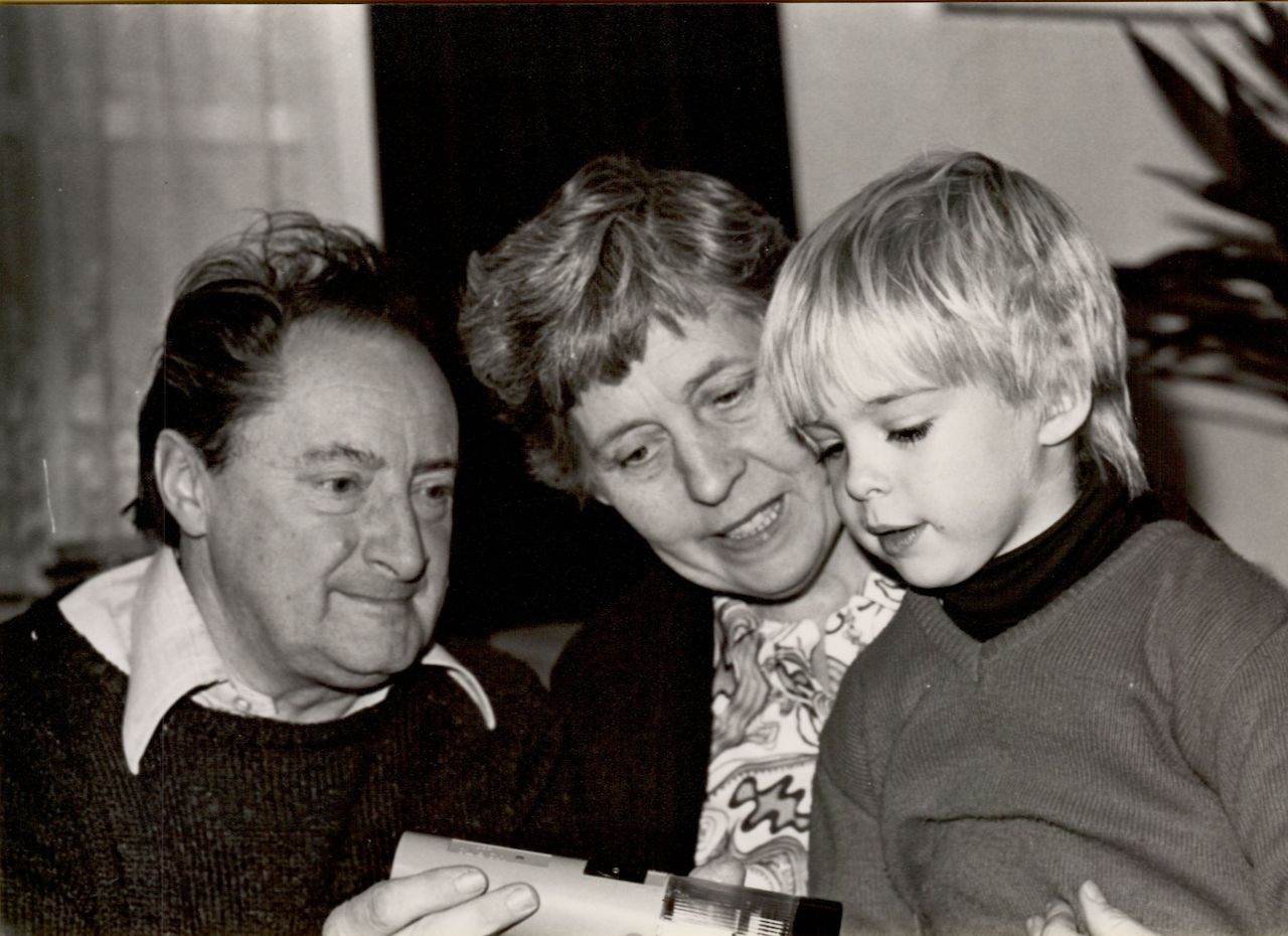 A child looks at a flashlight gift while sitting with two older adults, who are smiling and engaged.