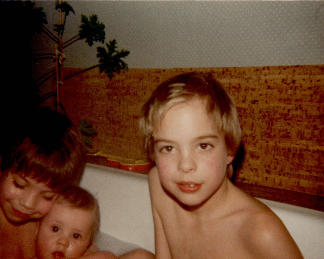 Three young children sitting together in a bathtub, looking at the camera.