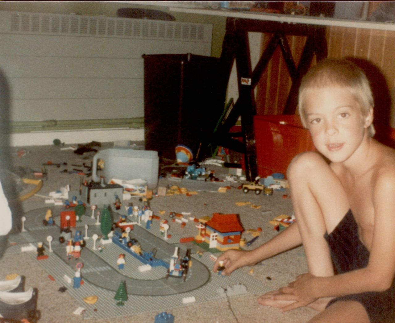 A young boy sits on the floor, playing with LEGO pieces and a toy city layout.