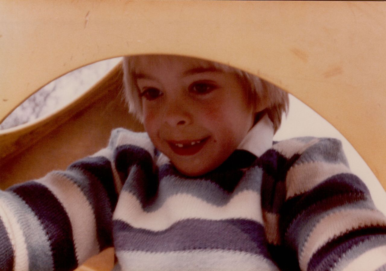 A smiling child in a striped sweater looks down while playing on a slide.