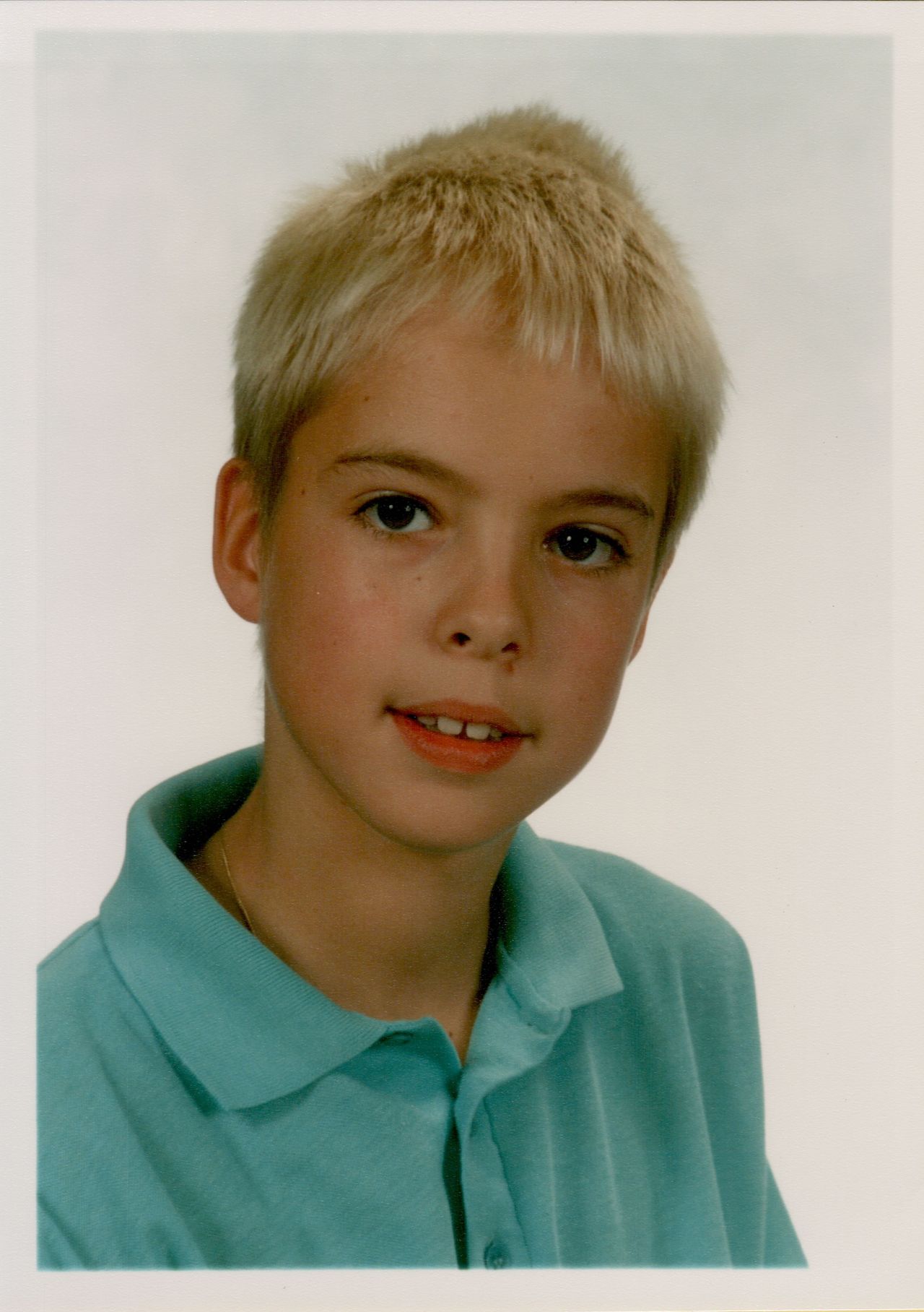 A young student with short blond hair wears a teal polo shirt and poses for a class photo.