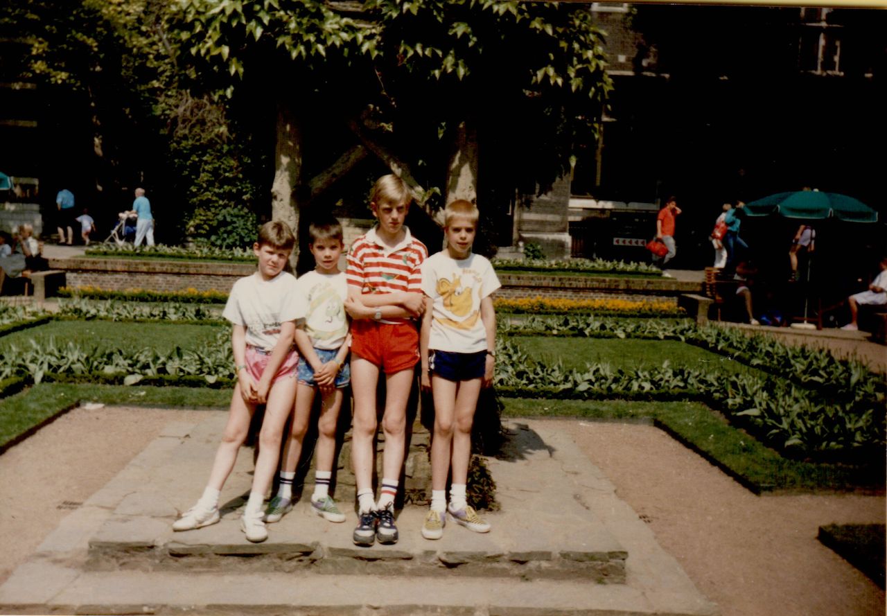 Four children stand together on a stone path in a garden, posing for a photo with serious expressions.