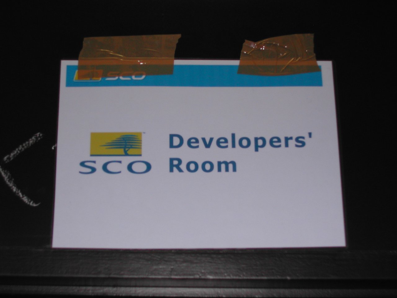 A printed sign reading "SCO Developers' Room" is taped to a dark surface, possibly as a joke or prank.