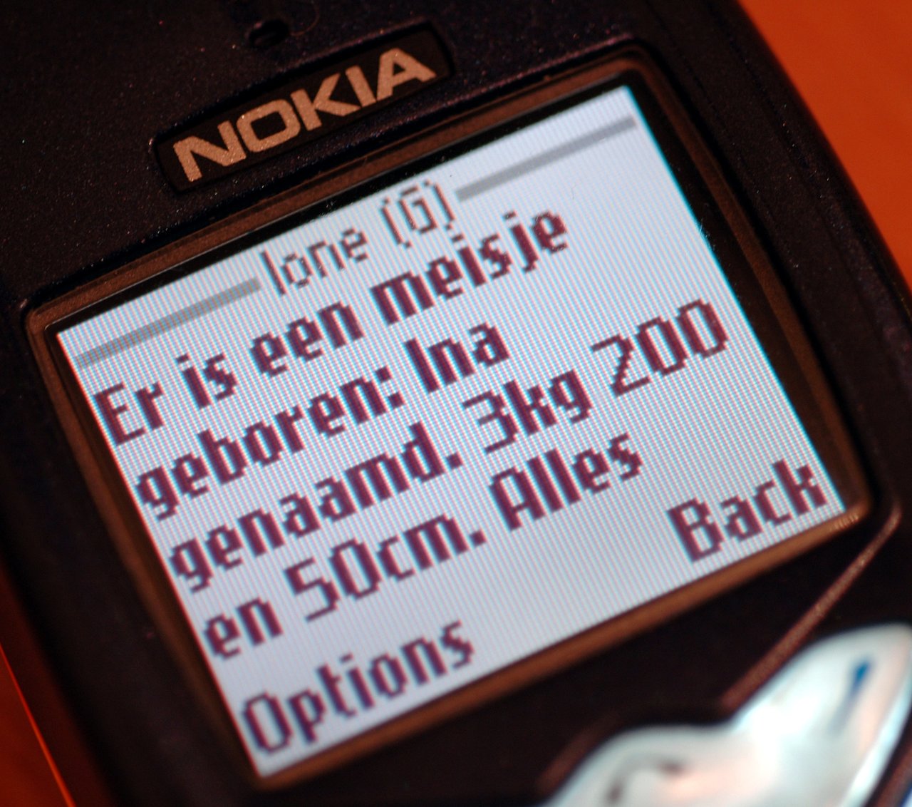 A Nokia phone screen displays a text message announcing the birth of a baby girl named Ina.
