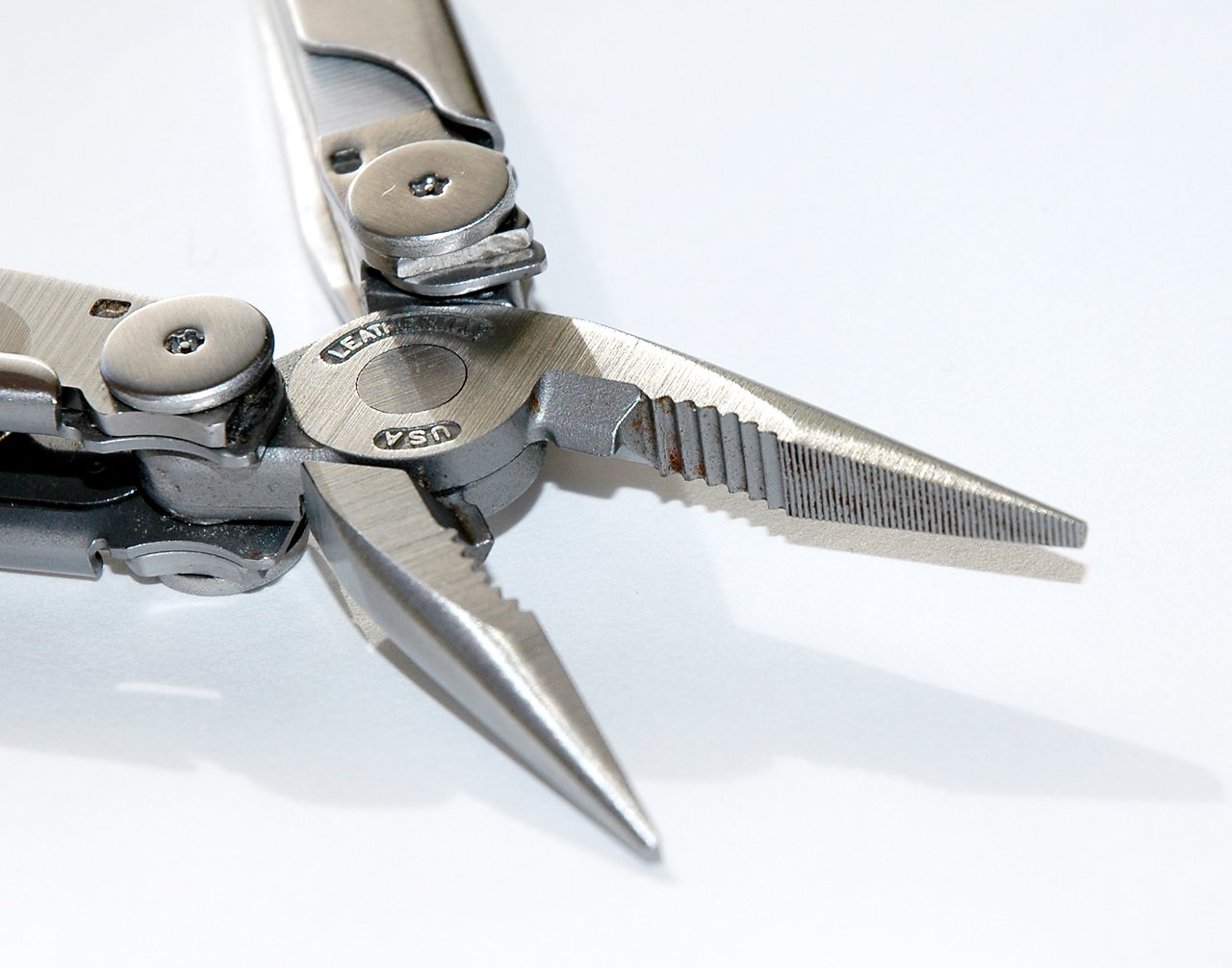 A close-up of a Leatherman multi-tool with its pliers open, showing metal details and slight rust on the jaws.