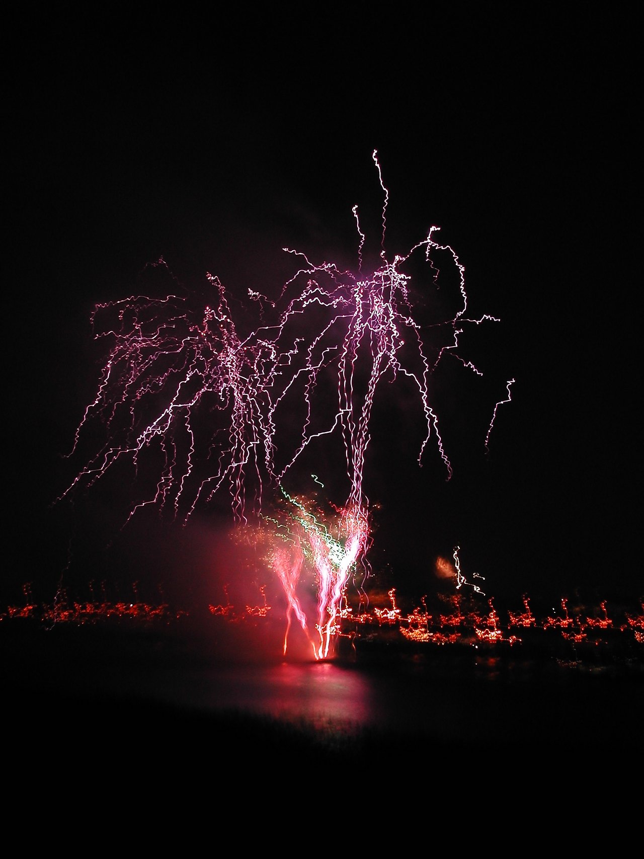 Fireworks light up the night sky over water, celebrating New Year's Eve.