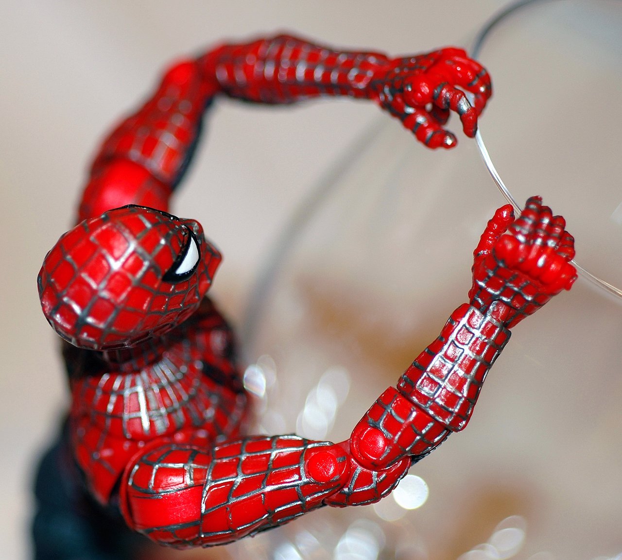 A close-up of a Spider-Man action figure gripping the edge of a clear surface with both hands.