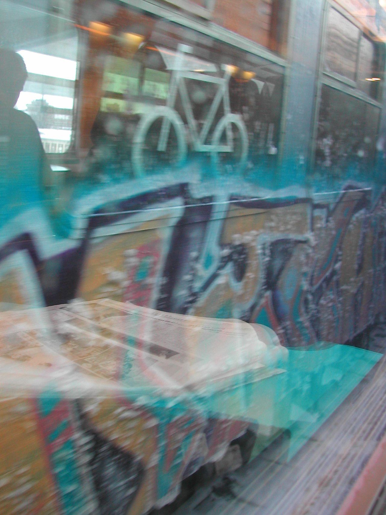 A train with graffiti passes by, reflected in a window while a newspaper rests on a table.