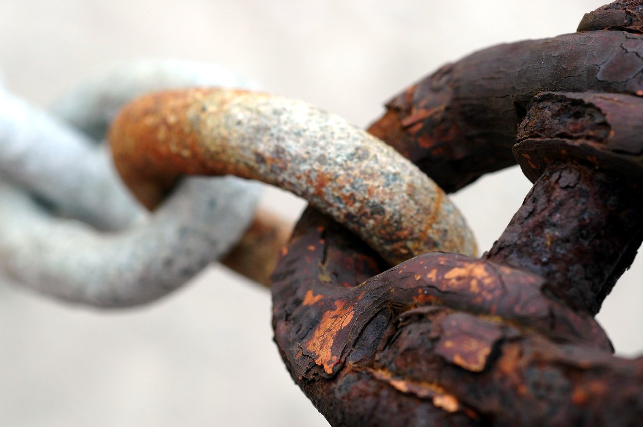 Close-up of interlocked metal chain links, showing varying degrees of rust and corrosion on the surface.