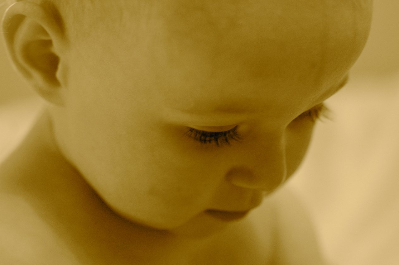 Close-up of a baby's face looking downward with soft lighting and a warm color tone.