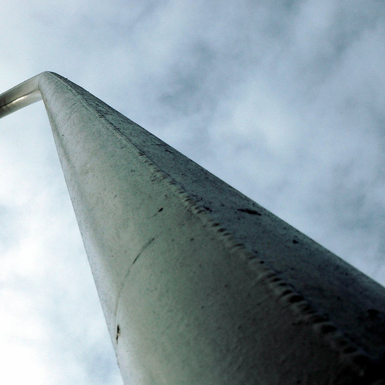 A tall metal pole photographed from below against a cloudy sky.