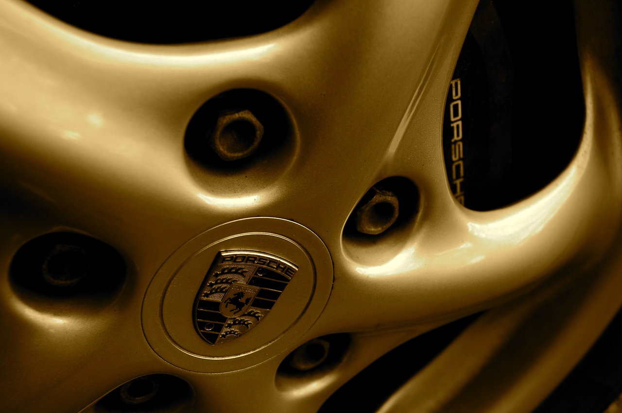 Close-up of a Porsche wheel, showing the emblem at the center and lug nuts around it.