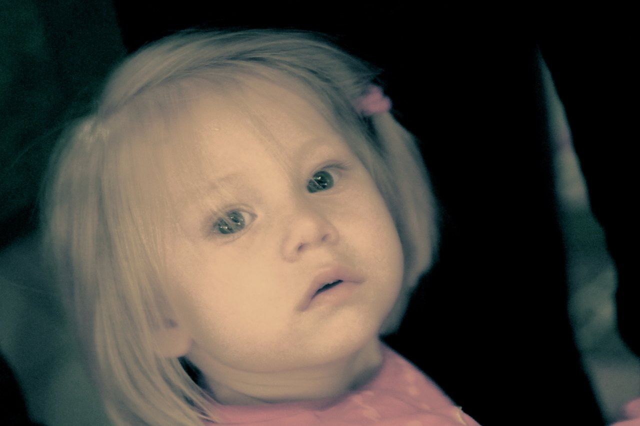 A young child with light hair and a pink outfit looks up with a curious expression.