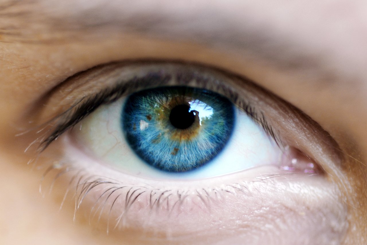 Close-up of a blue-green human eye with a reflection of a person taking a photo in the pupil.