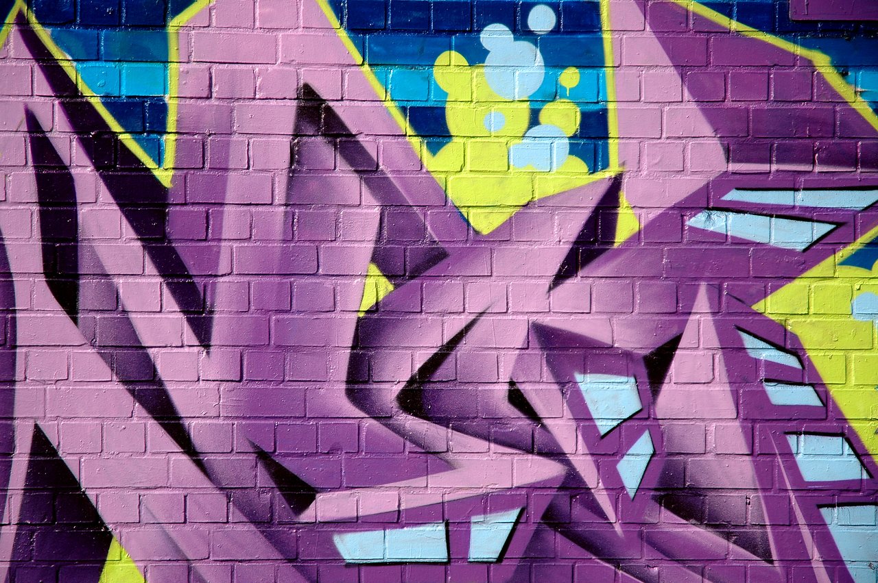 Bright graffiti with bold purple, blue, and yellow shapes painted on a brick wall.