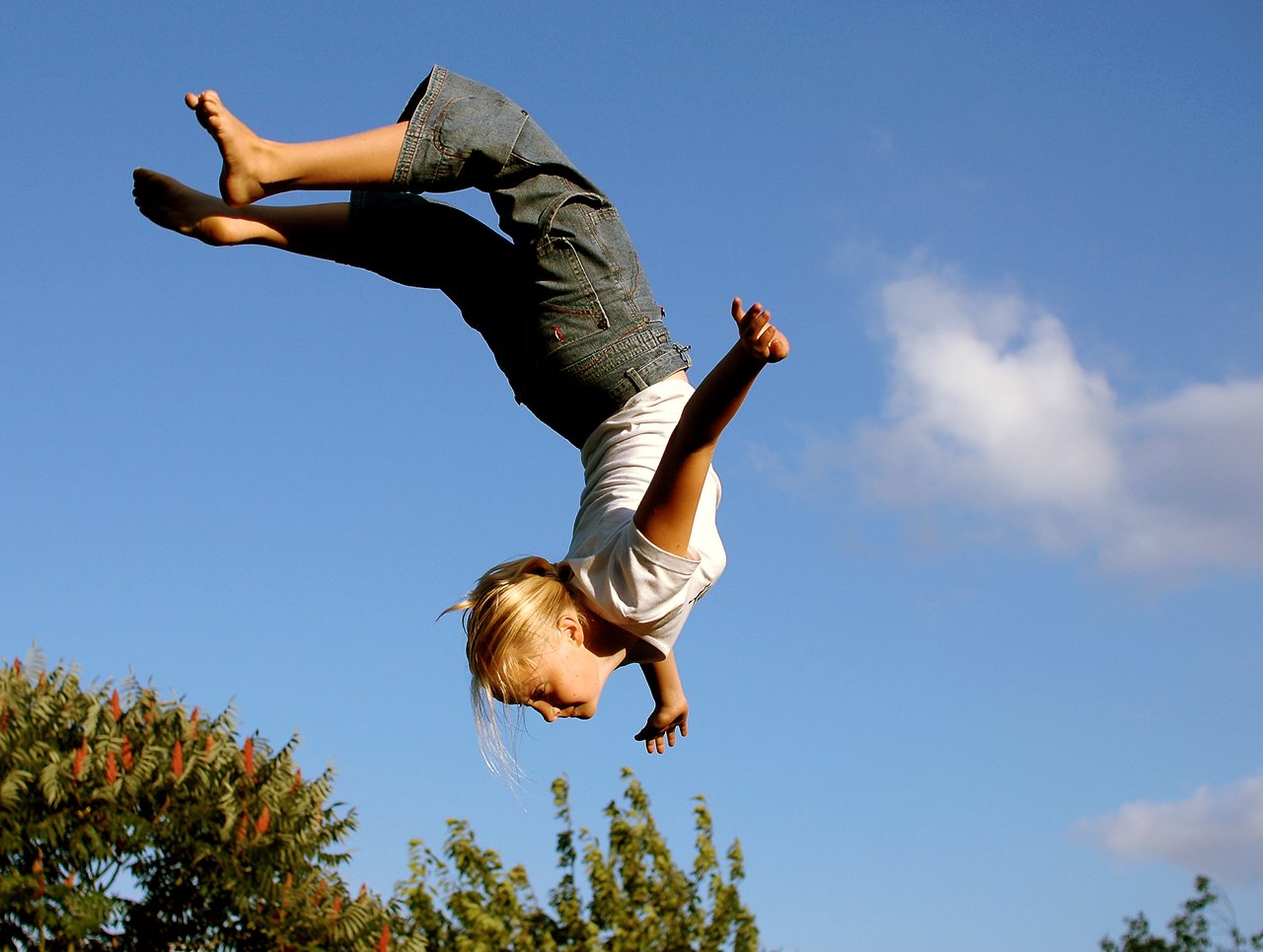 A person is upside down in mid-air with arms extended and legs bent against a clear blue sky.