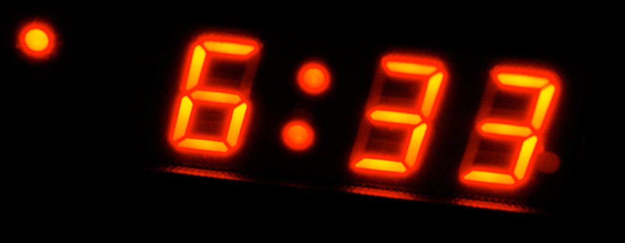 A digital clock displays 6:33 AM in red numbers in a dark room.