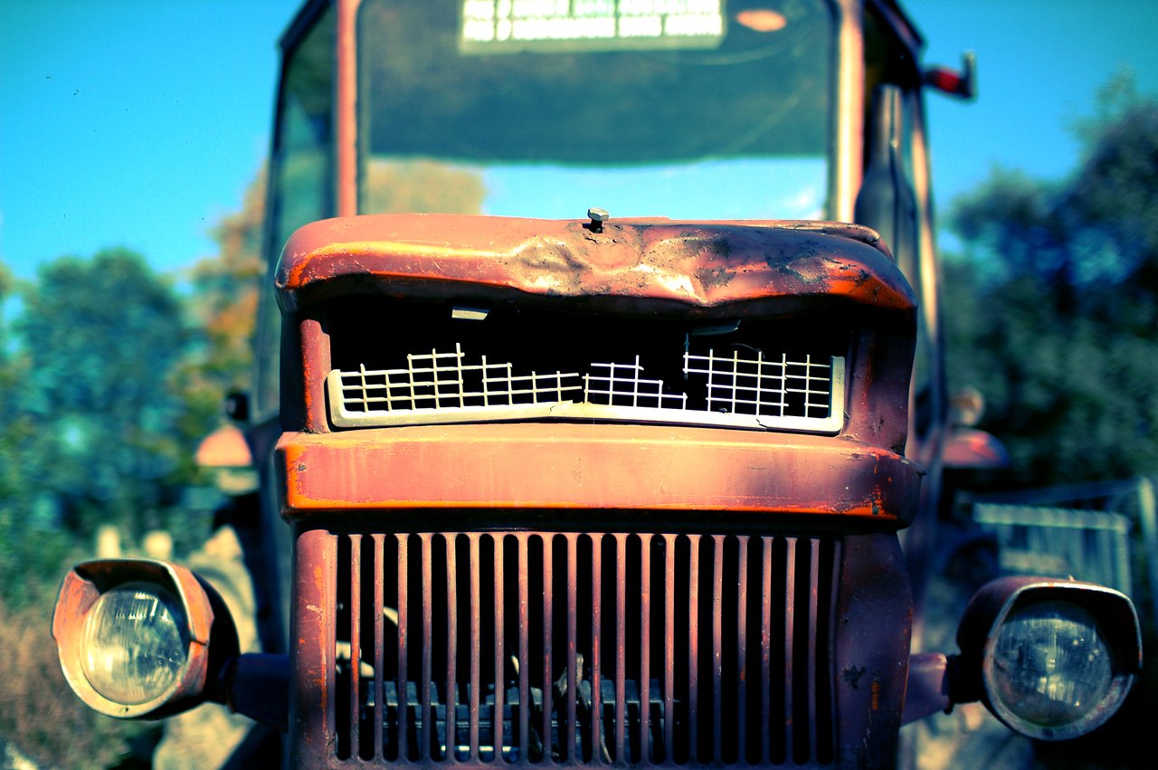 Close-up of an old, damaged tractor with a bent hood and broken front grille, parked outdoors.
