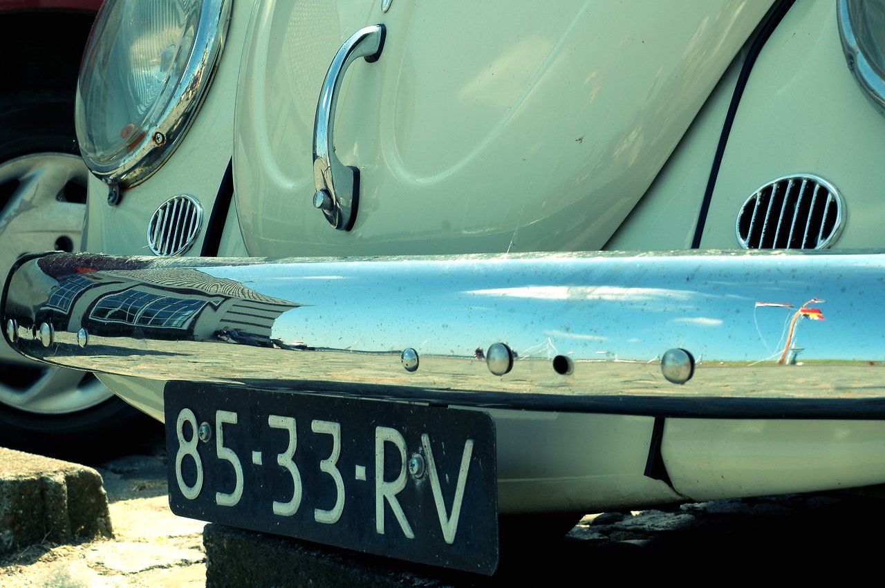 Close-up of a vintage Volkswagen Beetle's front bumper and license plate, with reflections visible on the chrome surface.
