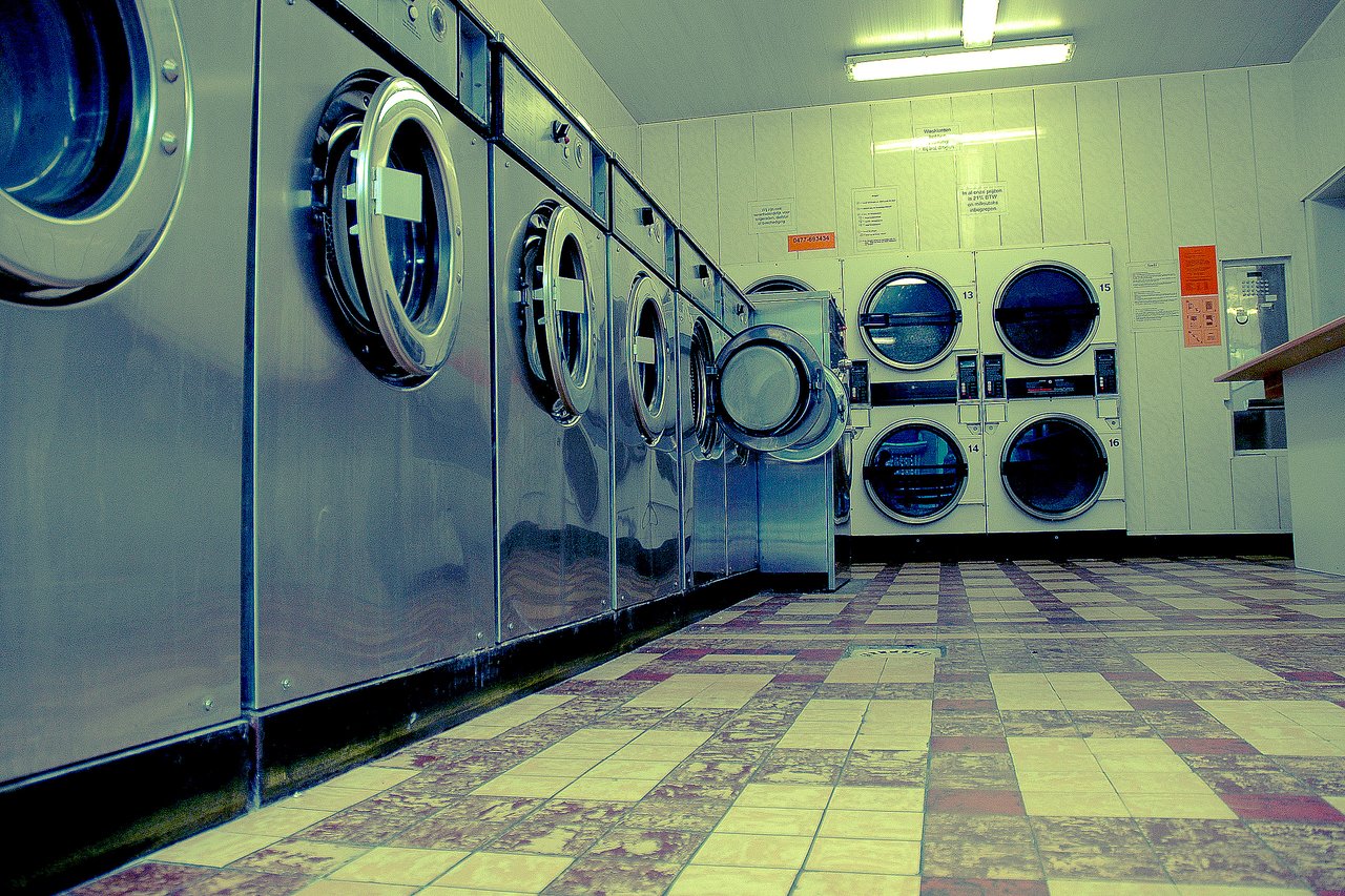 A laundromat with rows of stainless steel washing machines and dryers, one machine door open in the center.