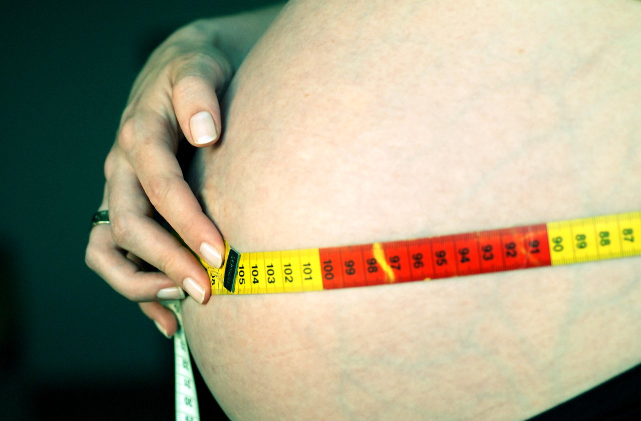 A hand measures a pregnant belly with a tape measure, showing 105 cm (about 41 inches).