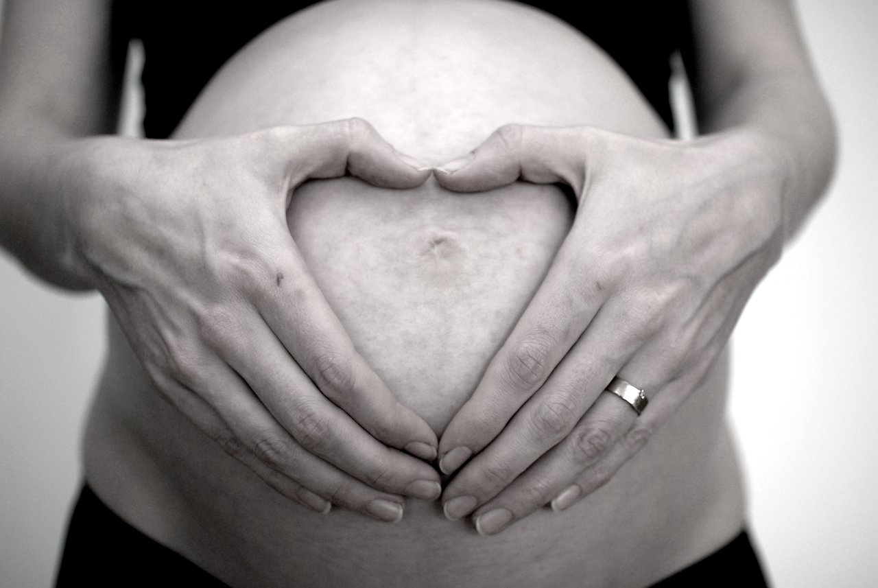A person forms a heart shape with their hands over their pregnant belly.