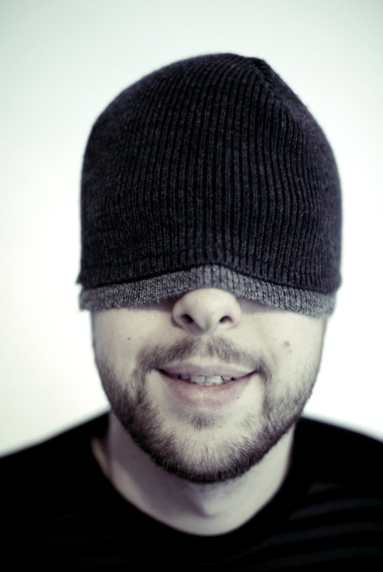 A man with a beanie pulled over his eyes smiles slightly, covering his vision.