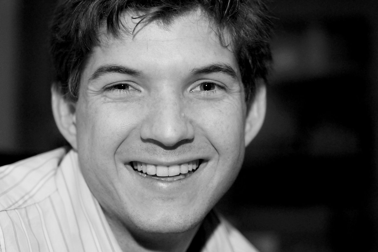 A smiling man in a striped shirt at a New Year's Eve gathering, moments before spilling a cocktail on himself.