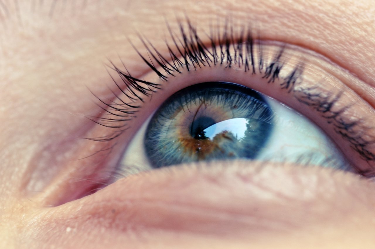 Close-up of a human eye with long eyelashes, reflecting light and surroundings in the iris.