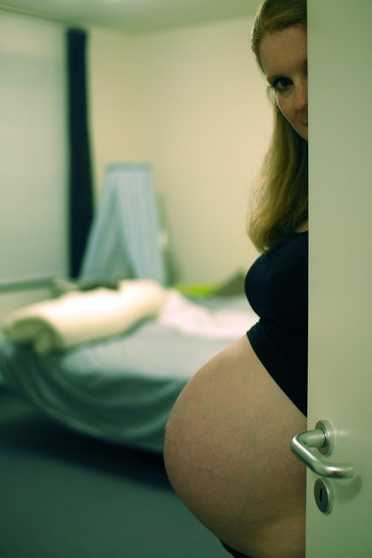 A pregnant woman peeks from behind a door, showing her baby bump.