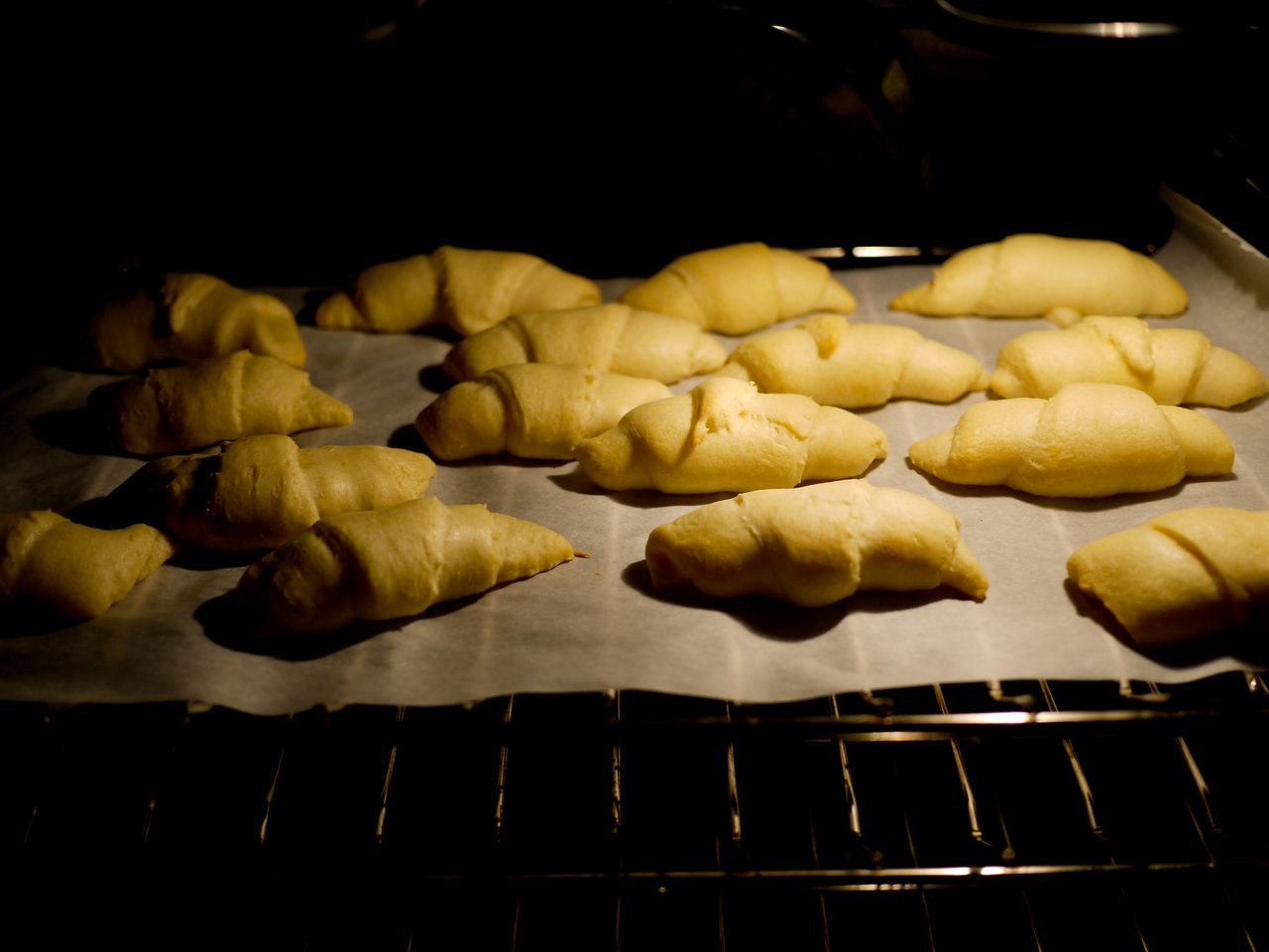 Partially baked croissants on a parchment-lined baking sheet inside an oven.