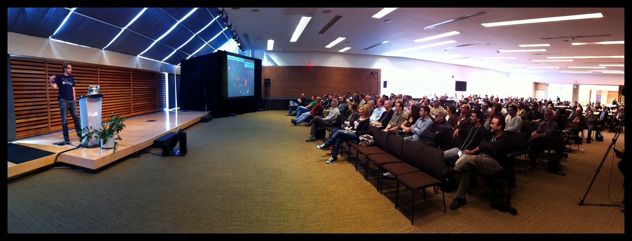 A speaker presents on stage at DrupalCamp Toronto while a large audience listens attentively.