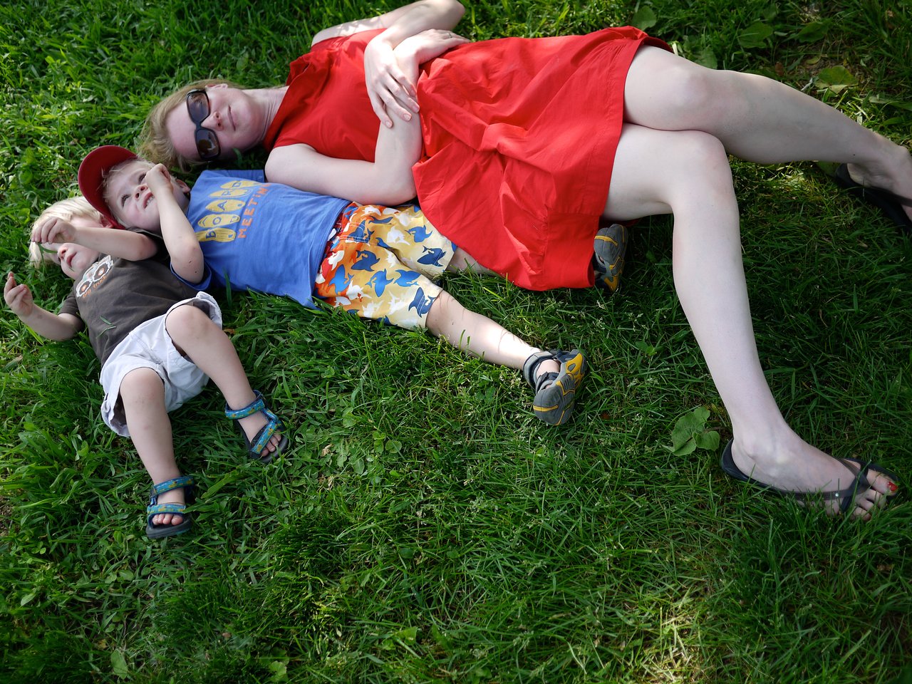 A woman and two children lie on the grass, relaxing together.