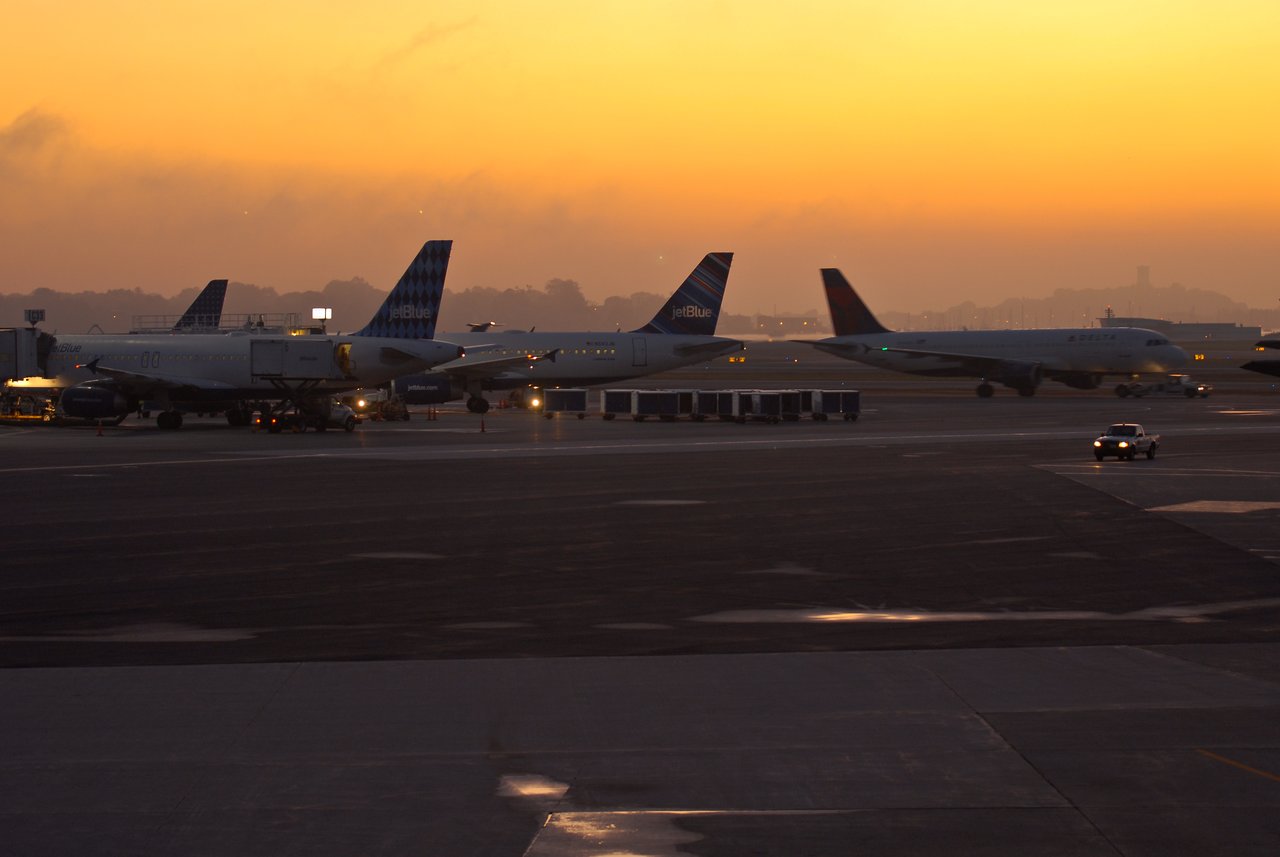 Several airplanes are parked at Logan Airport during dawn, with a warm sky in the background.