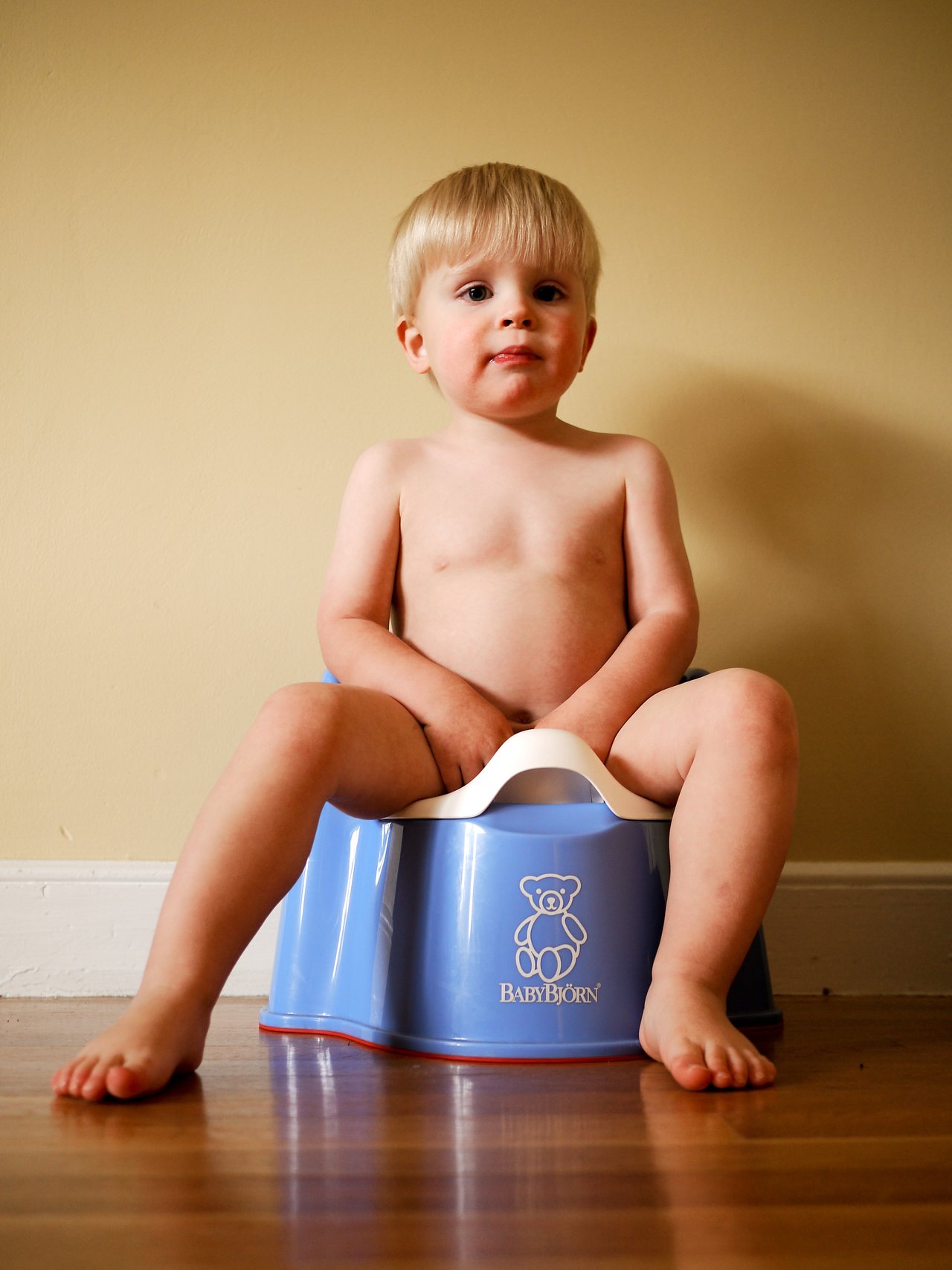 A young child sits on a blue potty, looking forward during potty training.