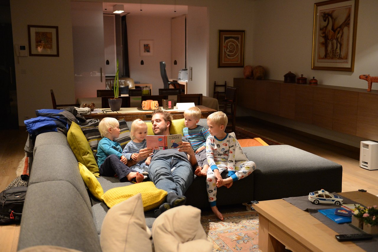 A man reads a bedtime story to four young children sitting with him on a couch.