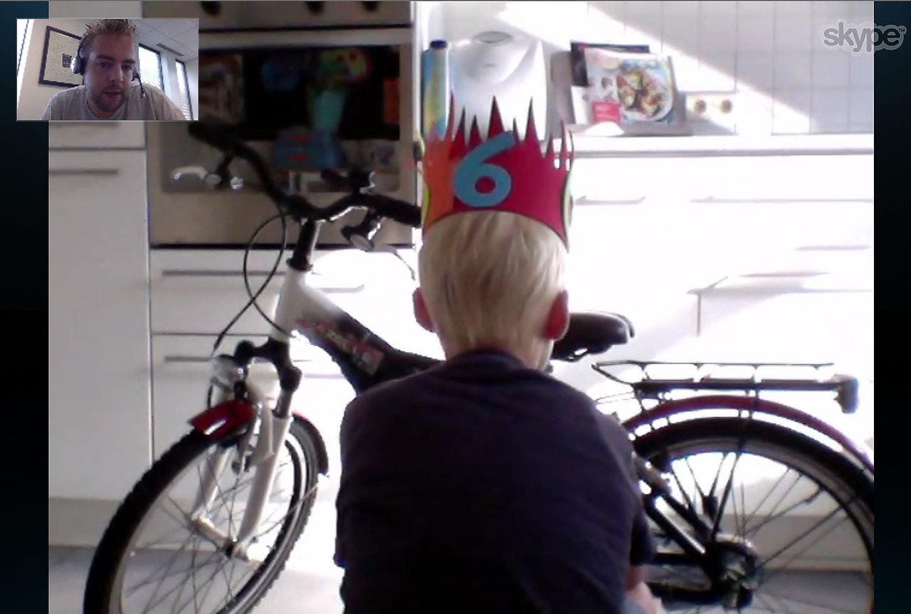 A child wearing a birthday crown with the number six sits in front of a new bicycle during a Skype call.