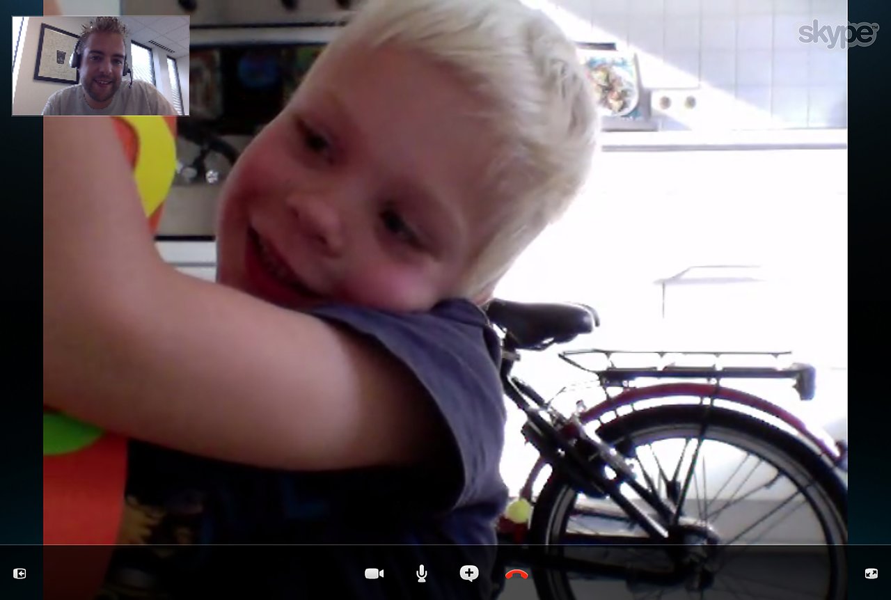 A child excitedly hugs a colorful gift while video calling an adult who is smiling in the corner.