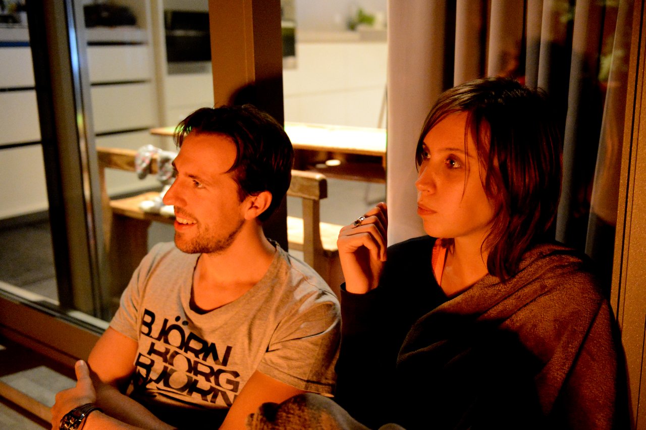 A man and a woman sit together indoors at night.