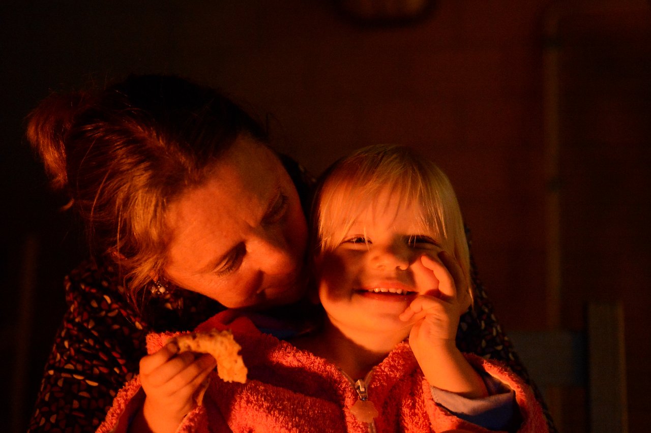 A woman and a smiling child sit close together, illuminated by warm light.