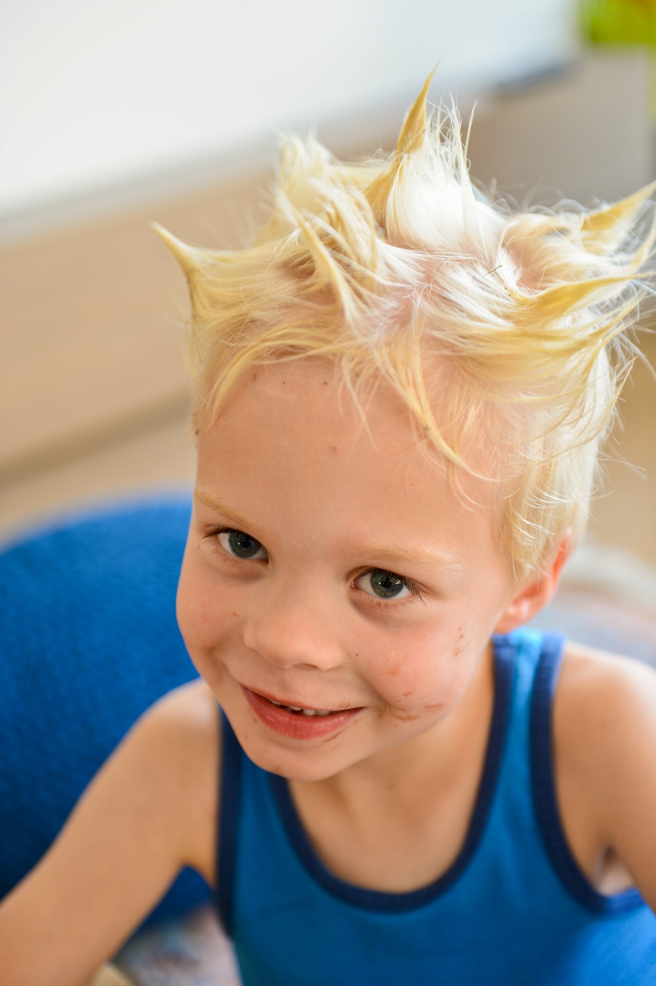 A young child with spiky blonde hair smiles while wearing a blue tank top.