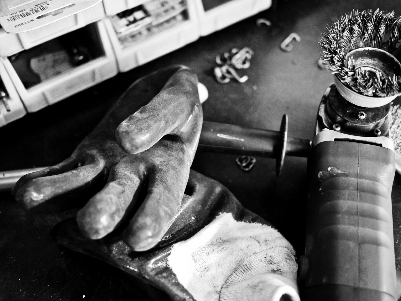 A worn work glove rests on a table beside a power tool with a wire brush attachment.