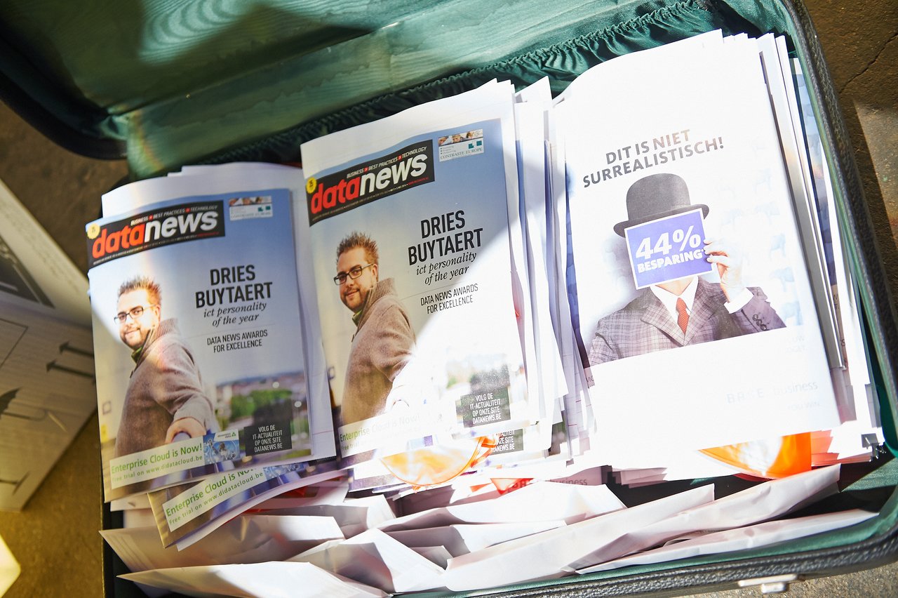 A stack of Data News magazines featuring Dries Buytaert as ICT Personality of the Year, placed inside an open suitcase.