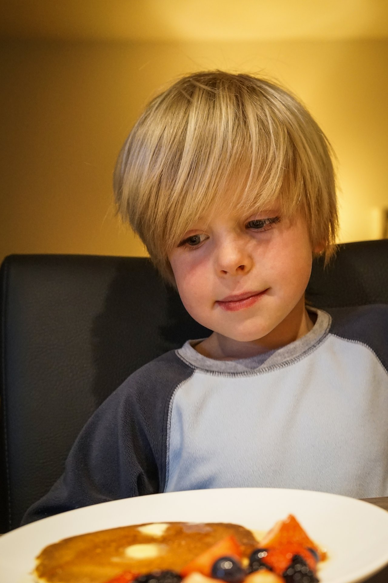 A young child looks at a plate of American pancakes with butter and fresh berries.