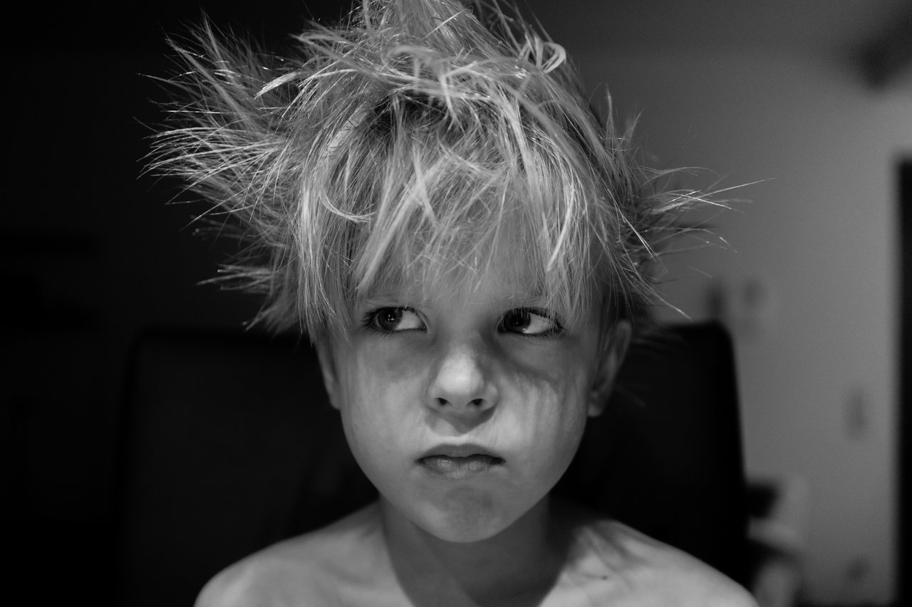 A young child with messy, spiky hair looks to the side with a serious expression.