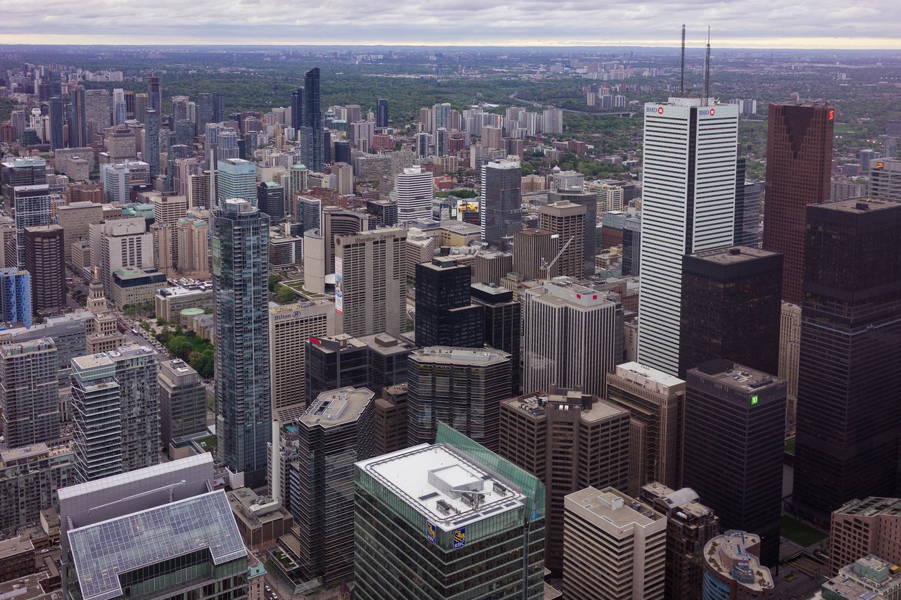 Aerial view of downtown Toronto with tall skyscrapers and city buildings stretching toward the horizon under a cloudy sky.