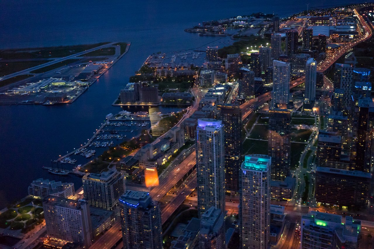 Aerial view of downtown Toronto at night, showing illuminated skyscrapers, roads, and waterfront with a small airport.