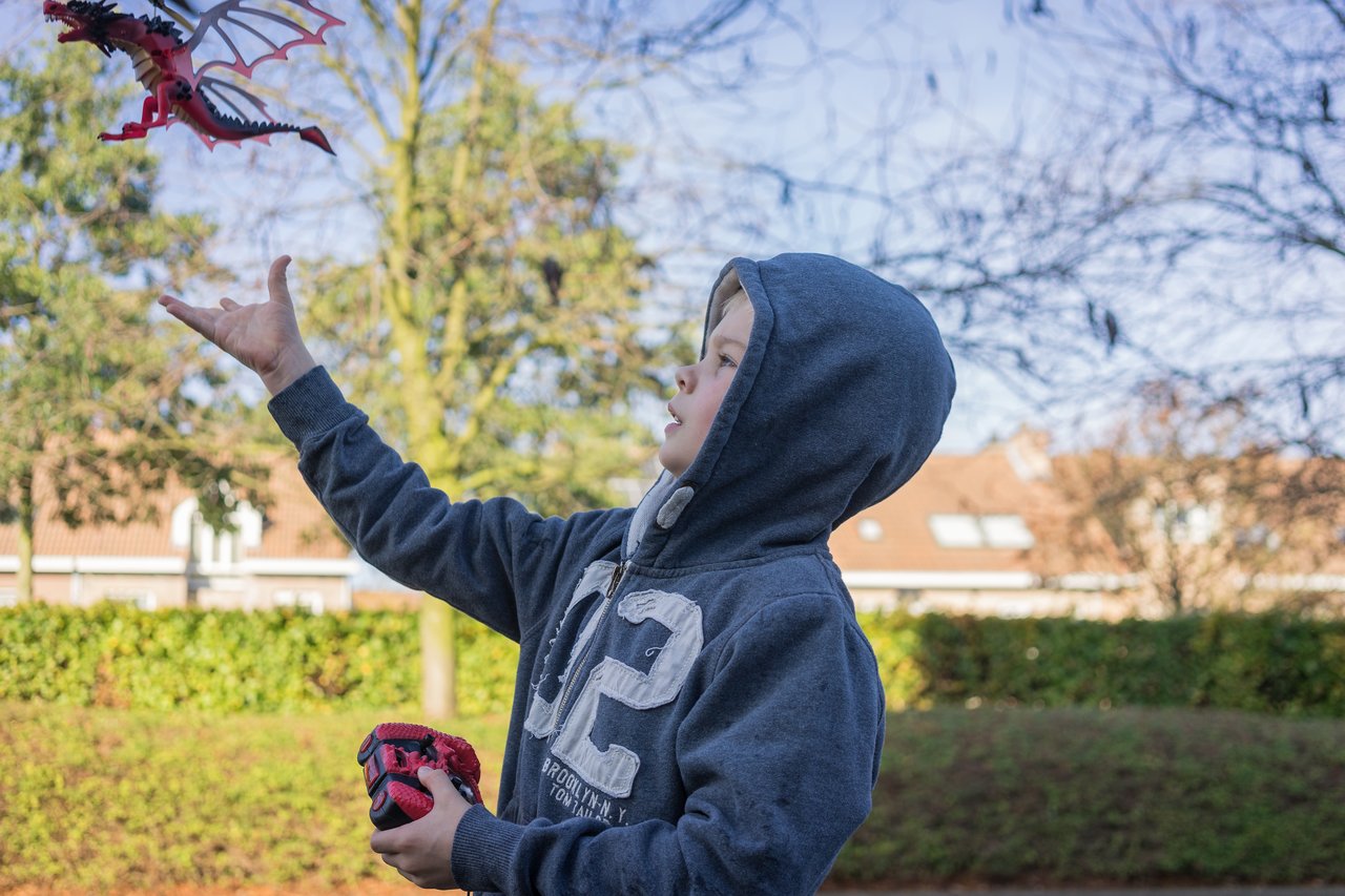 A child in a hoodie launches a flying dragon toy into the air while holding a controller in one hand.