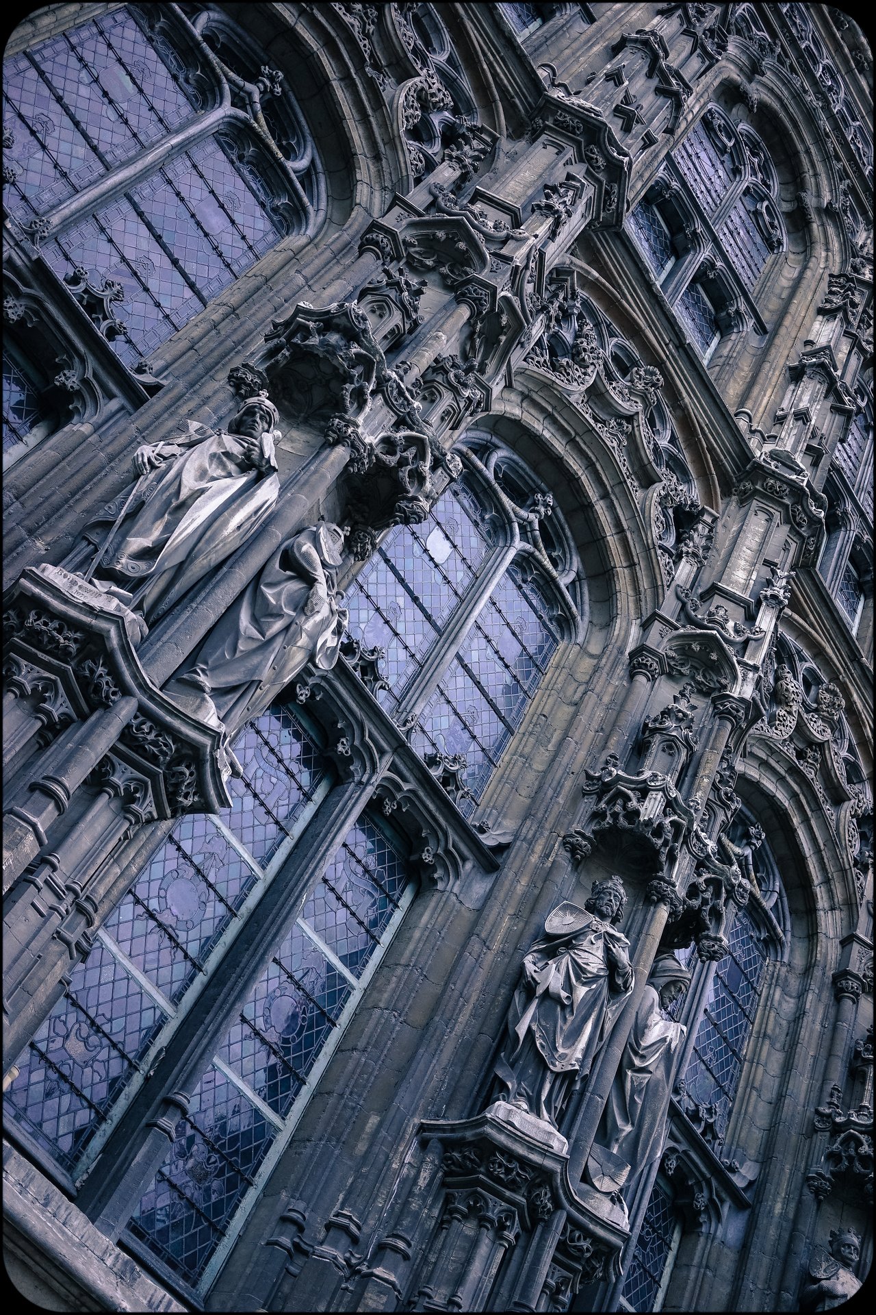 Ornate Gothic building facade in Ghent with detailed stone statues and large stained-glass windows.