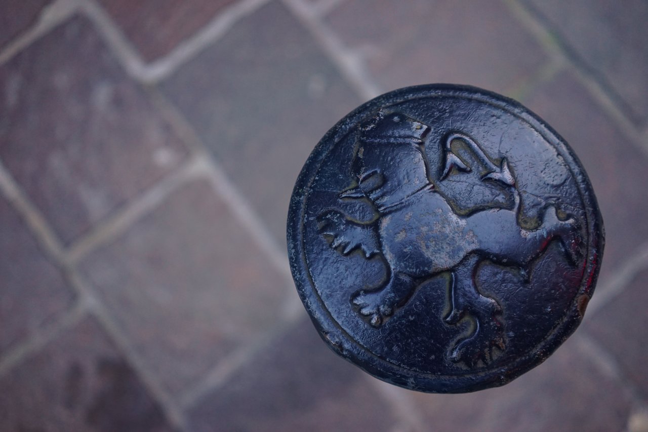 A metal post with a raised lion emblem on top, set against a stone pavement background.
